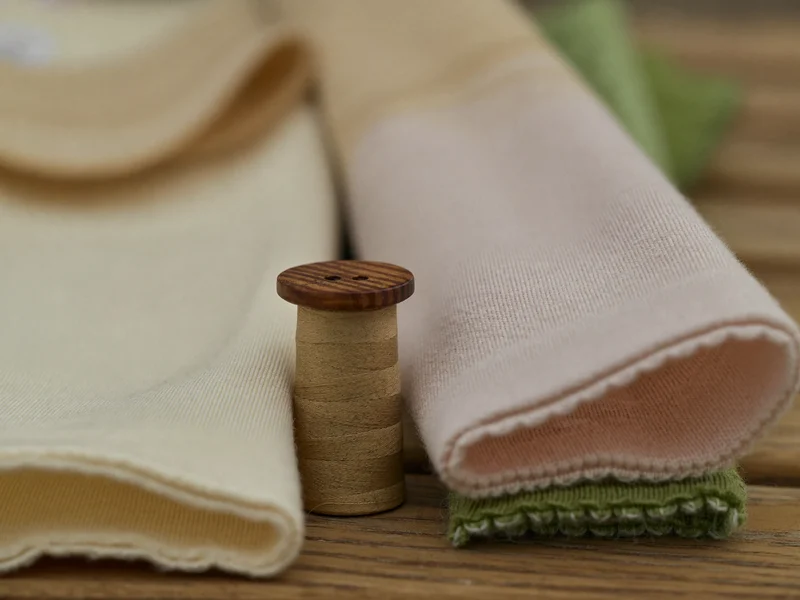 Gros plan sur des échantillons de jersey et de maille, un bouton en bois et une bobine.