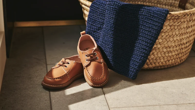 Petites chaussures d'enfant et pull plié près d'un panier tressé, dans une entrée ensoleillée.
